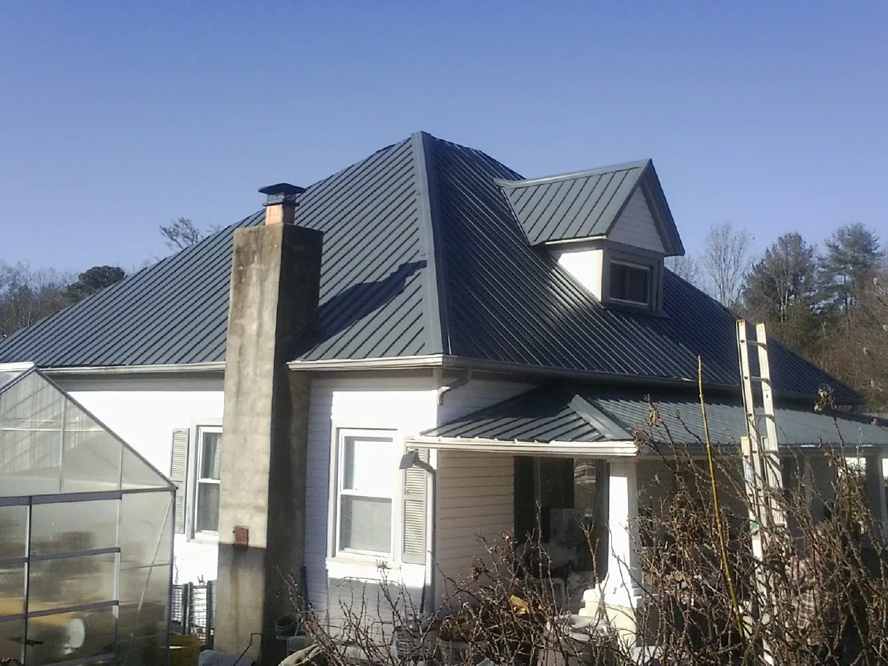Dark blue standing seam metal roof on a white farmhouse with dormer — Slate & Tile Roof Repair by Roofing Brothers in Kilgore