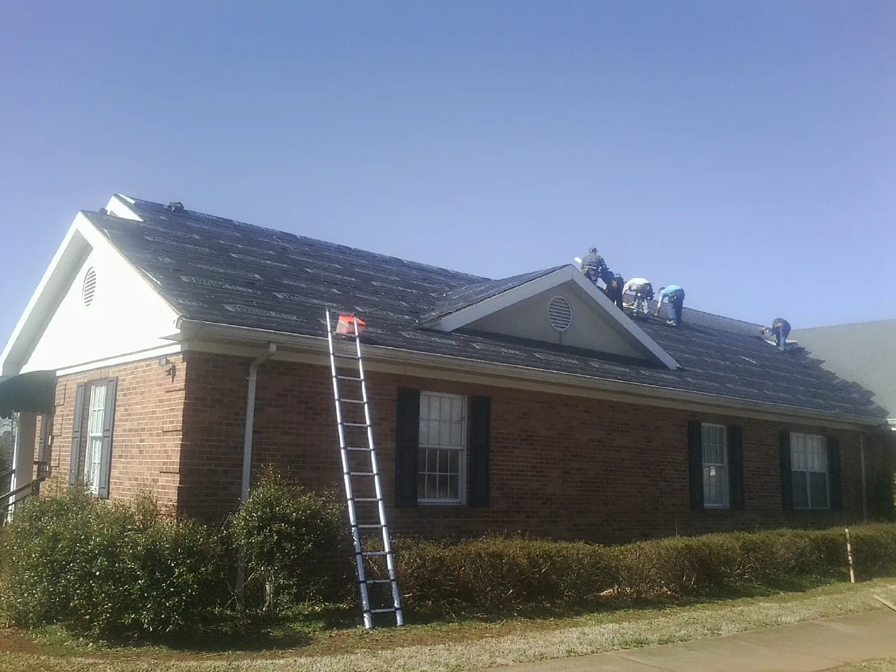 Crew tearing shingles off a brick ranch roof with a ladder set — Metal Roof Repair work by our crew in Kilgore