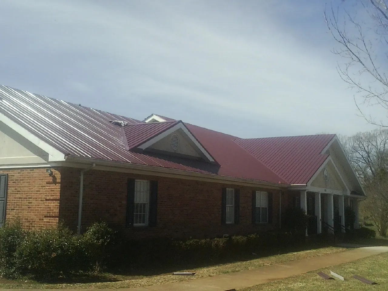 Red metal roof with gabled entries on a long brick building, from a Hail Damage Roof Repair job in Kilgore
