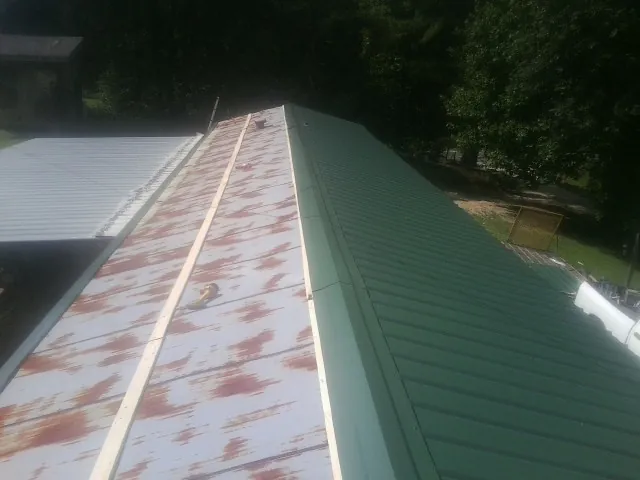 Old rusted panels beside newly installed green metal roofing — Wind Damage Roof Repair by Roofing Brothers in Kilgore