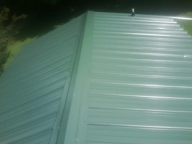 New green metal panels meeting at the ridge of a roof — Flat Roof Repair work by our crew in Kilgore