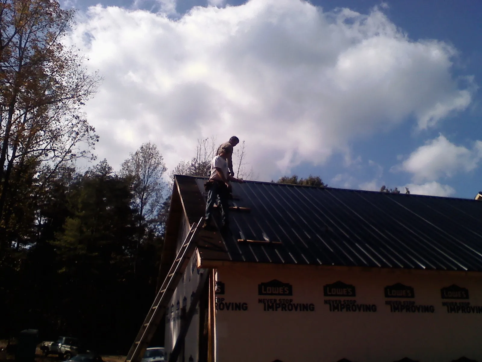 Roofer fastening dark metal panels high against a cloudy sky, from a Roof Inspection job in Kilgore