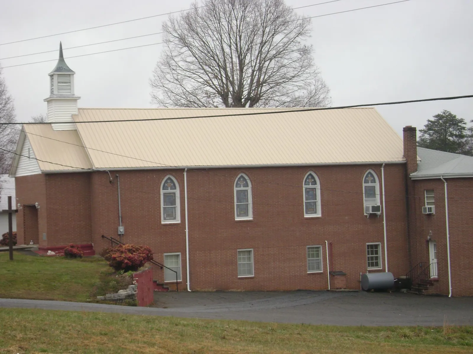 New tan metal roof on a brick church with a white steeple in Kilgore