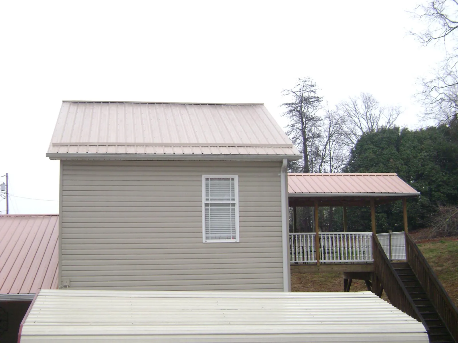 Tan metal roofs on a two story addition and attached porch, from a Roof Replacement job in Kilgore